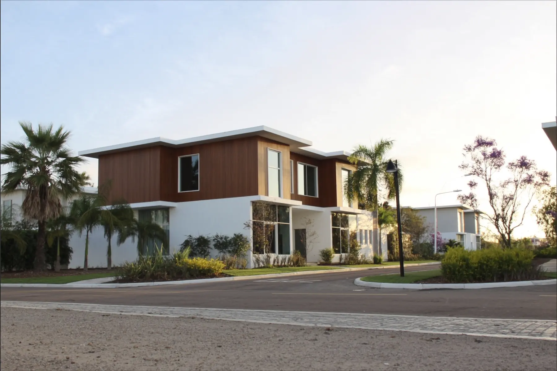 A modern two-storey house in white and timber, on a tree-lined residential street at sunset